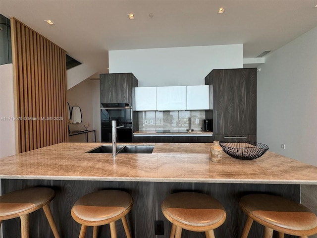 kitchen featuring a center island, sink, double oven, tasteful backsplash, and a breakfast bar area