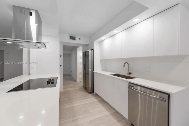 kitchen with white cabinets, stainless steel appliances, wall chimney range hood, and sink