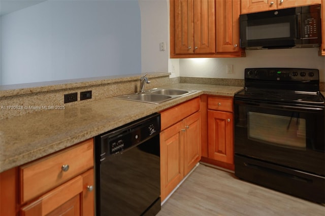 kitchen featuring black appliances, light hardwood / wood-style floors, light stone counters, and sink