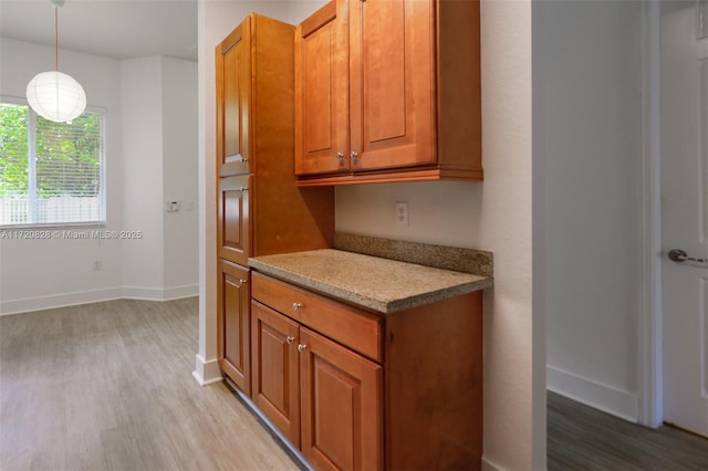 kitchen with light stone countertops, hanging light fixtures, and light hardwood / wood-style flooring