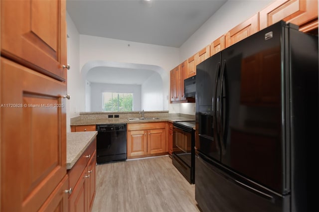 kitchen featuring black appliances, light hardwood / wood-style floors, light stone counters, and sink