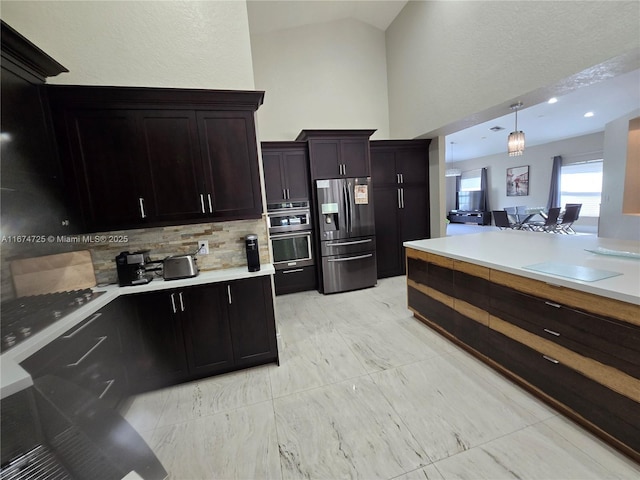 kitchen featuring decorative backsplash, appliances with stainless steel finishes, dark brown cabinetry, hanging light fixtures, and lofted ceiling