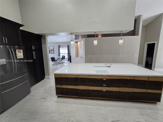 kitchen with a center island with sink, black fridge with ice dispenser, hanging light fixtures, and a textured ceiling