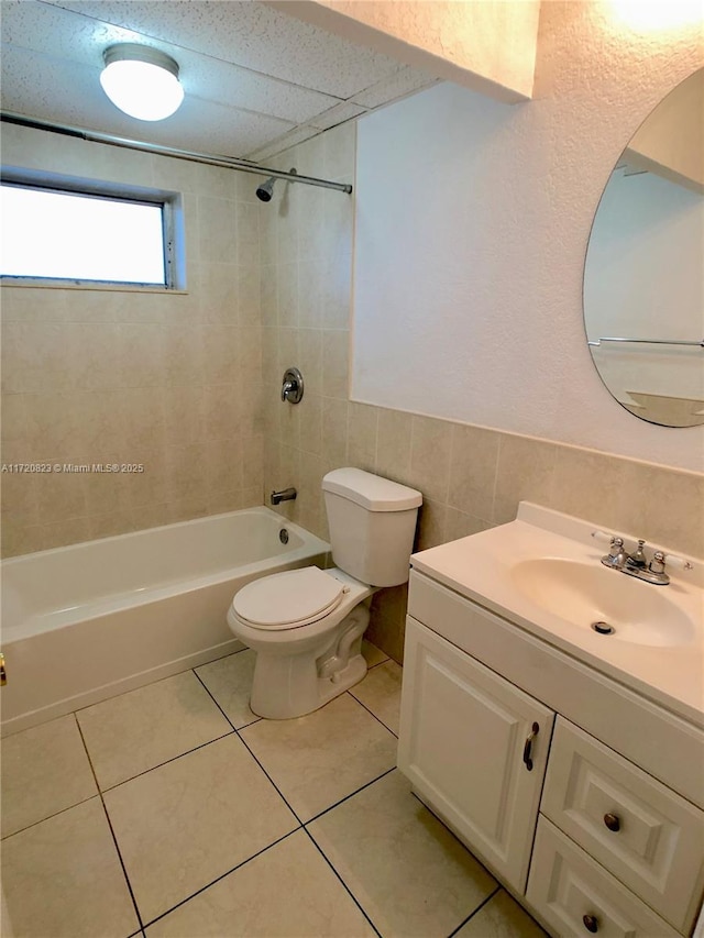 full bathroom with tiled shower / bath combo, tile patterned flooring, toilet, vanity, and tile walls