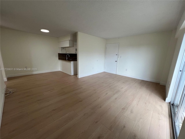 unfurnished living room featuring hardwood / wood-style flooring, sink, and a textured ceiling