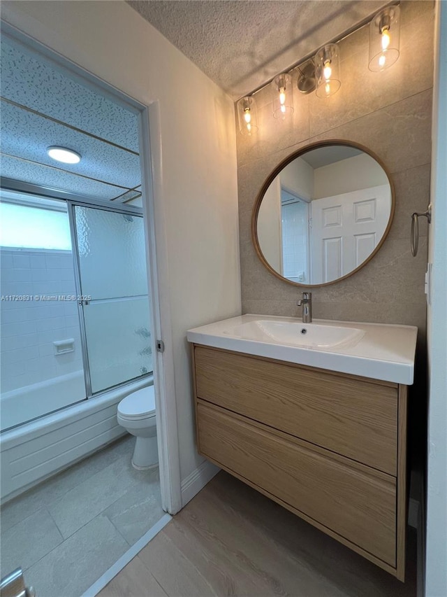 full bathroom with vanity, a textured ceiling, toilet, and enclosed tub / shower combo