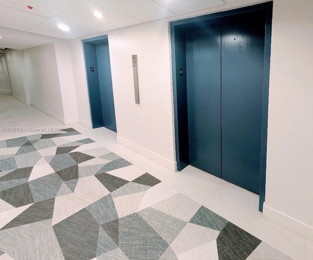 hallway with baseboards, a paneled ceiling, and elevator