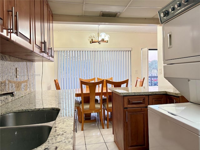 kitchen featuring sink, light tile patterned floors, decorative light fixtures, an inviting chandelier, and stacked washer and dryer