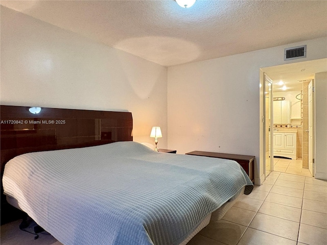 tiled bedroom featuring ensuite bathroom and a textured ceiling