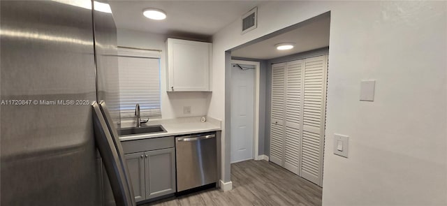 kitchen with stainless steel dishwasher, gray cabinetry, sink, white cabinets, and light hardwood / wood-style floors