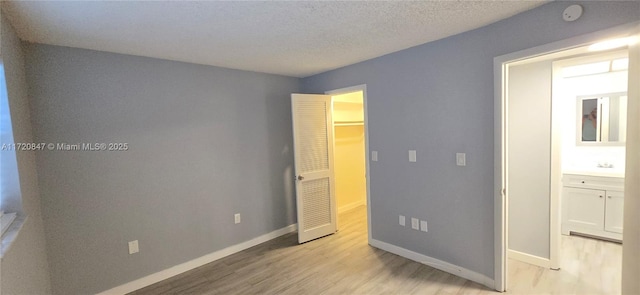 unfurnished bedroom with a textured ceiling, light wood-type flooring, a spacious closet, and sink