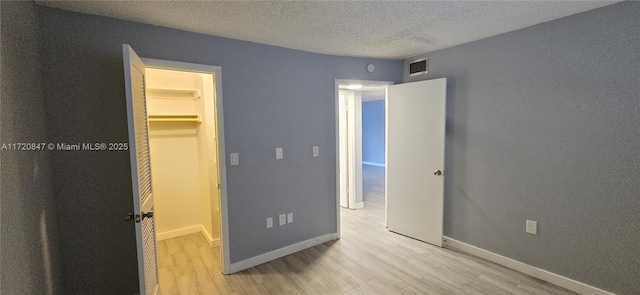 unfurnished bedroom with a walk in closet, a closet, light hardwood / wood-style floors, and a textured ceiling