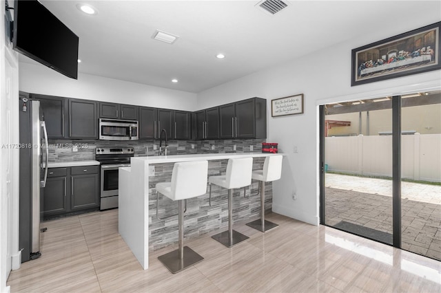 kitchen featuring a kitchen bar, appliances with stainless steel finishes, backsplash, and light tile patterned floors