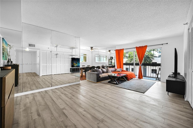 living room featuring ceiling fan, light hardwood / wood-style floors, and a textured ceiling