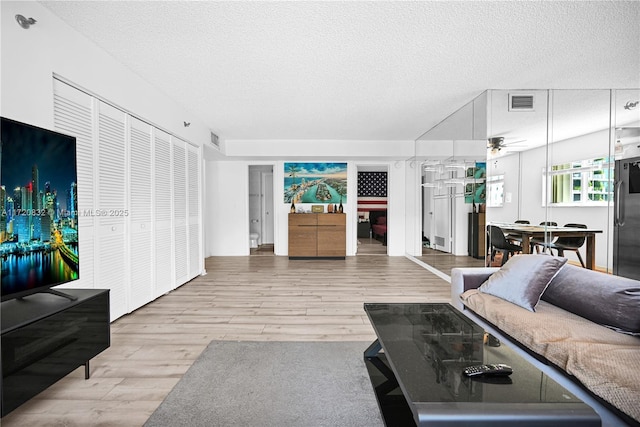 living room featuring ceiling fan, light hardwood / wood-style floors, and a textured ceiling