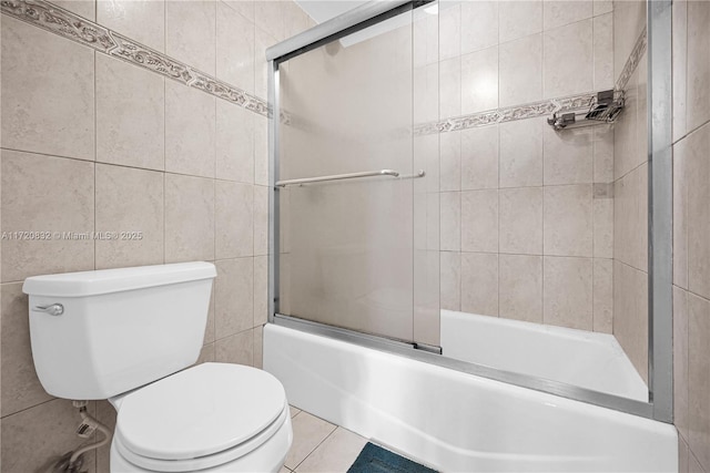 bathroom with shower / bath combination with glass door, tile patterned flooring, tile walls, and toilet