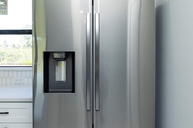 details with white cabinets, stainless steel fridge, and light stone countertops