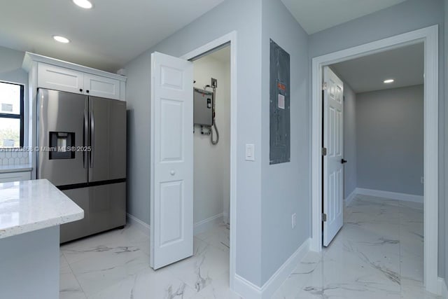 kitchen with electric panel, stainless steel fridge with ice dispenser, water heater, light stone counters, and white cabinetry