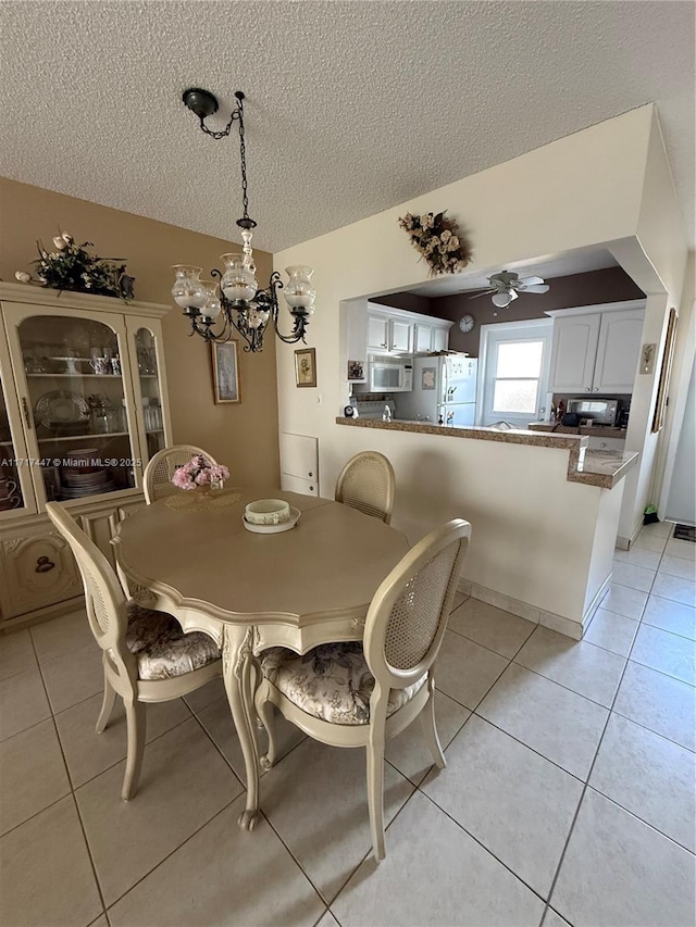 dining room with ceiling fan with notable chandelier, light tile patterned floors, and a textured ceiling