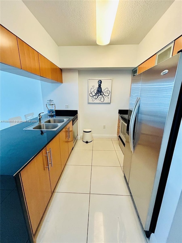 kitchen with dishwashing machine, freestanding refrigerator, a textured ceiling, a sink, and light tile patterned flooring