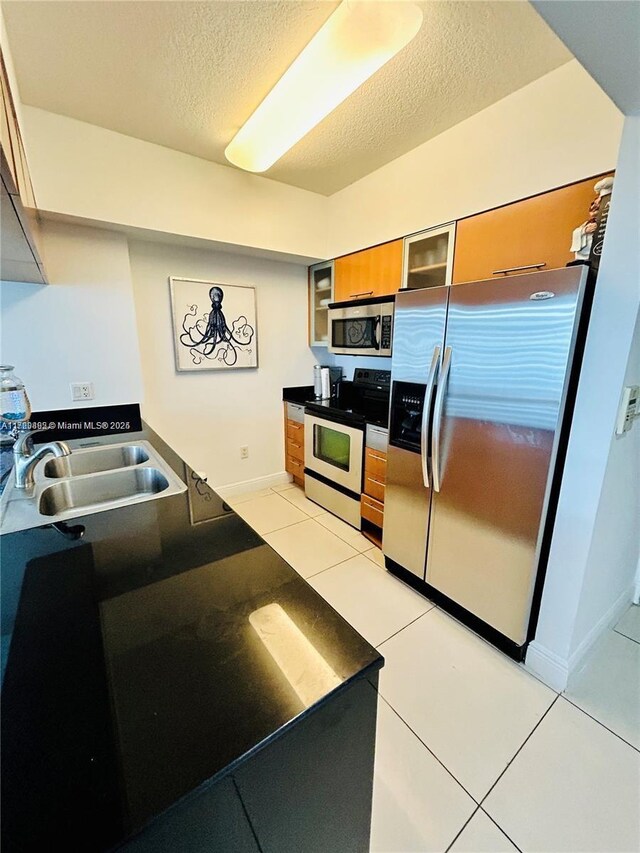 kitchen with a textured ceiling, sink, light tile patterned floors, and stainless steel appliances