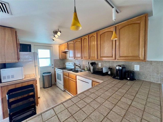 kitchen featuring visible vents, a sink, white appliances, decorative backsplash, and tile counters