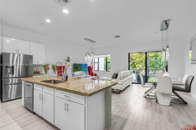 kitchen with sink, white cabinetry, stainless steel appliances, and an island with sink