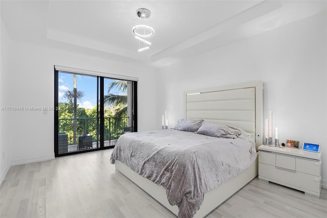 bedroom with a tray ceiling, light hardwood / wood-style flooring, and access to outside