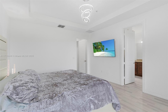 bedroom featuring a tray ceiling, ensuite bath, and light wood-type flooring