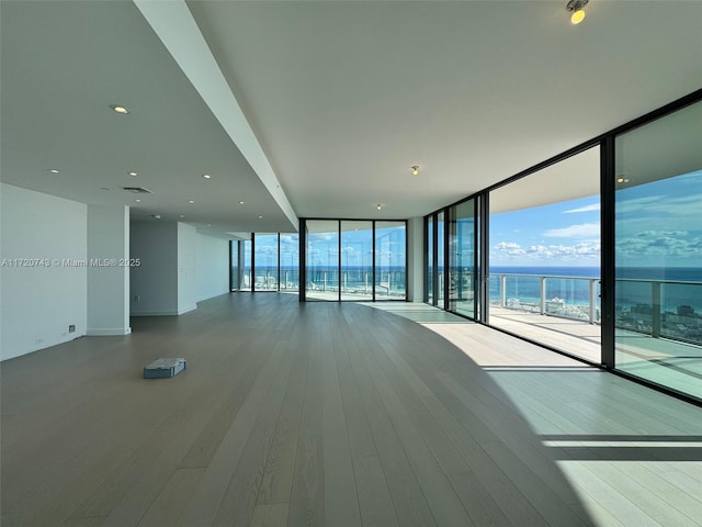 spare room with expansive windows, wood-type flooring, and a water view