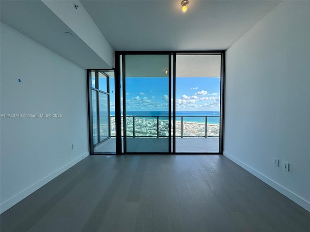 spare room with expansive windows, dark wood-style flooring, a water view, and baseboards