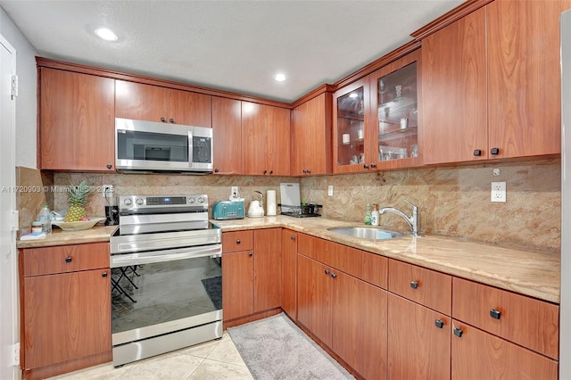 kitchen with sink, light tile patterned floors, tasteful backsplash, light stone counters, and stainless steel appliances