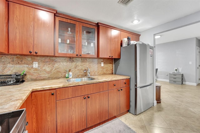 kitchen with sink, decorative backsplash, stainless steel fridge, light tile patterned flooring, and light stone counters