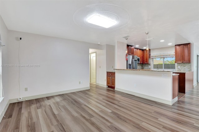 kitchen featuring pendant lighting, kitchen peninsula, decorative backsplash, stainless steel fridge, and light stone counters