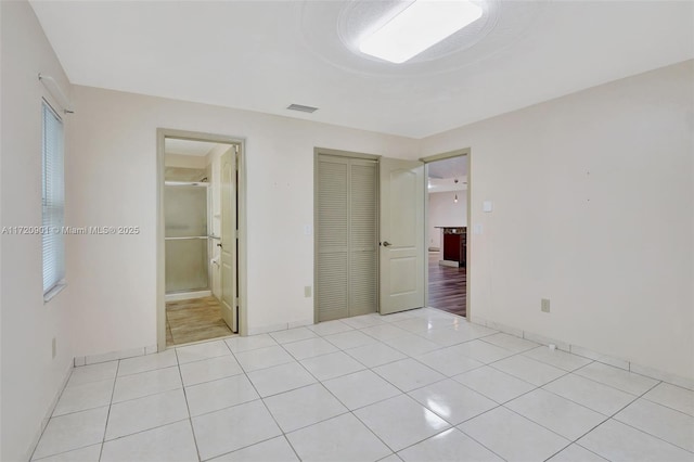 unfurnished bedroom with a closet, light tile patterned floors, and ensuite bath