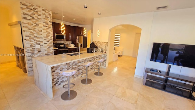 kitchen with dark brown cabinetry, stainless steel appliances, a peninsula, a kitchen breakfast bar, and pendant lighting