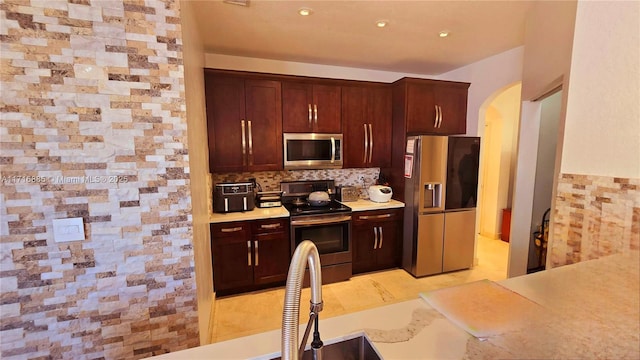 kitchen with arched walkways, light countertops, appliances with stainless steel finishes, and tasteful backsplash