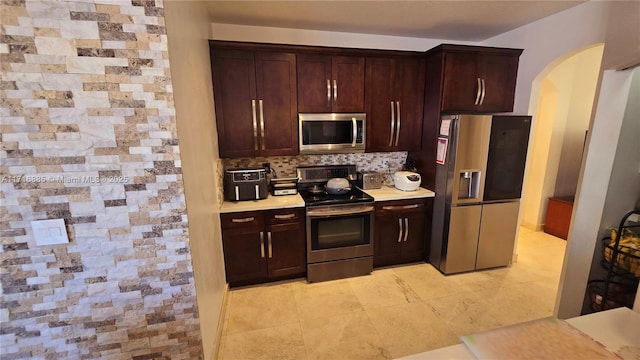 kitchen with arched walkways, decorative backsplash, appliances with stainless steel finishes, light countertops, and light tile patterned flooring