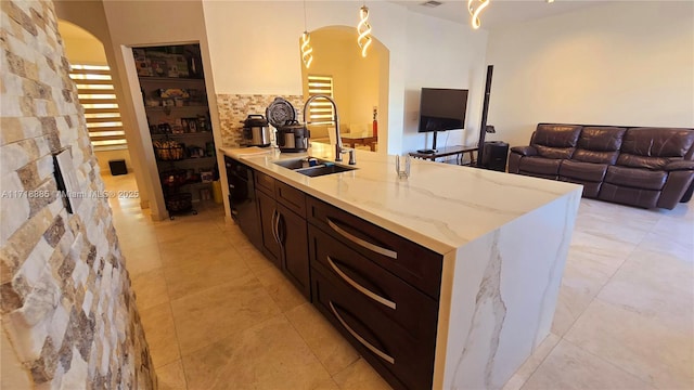 kitchen with arched walkways, pendant lighting, a sink, and light stone countertops