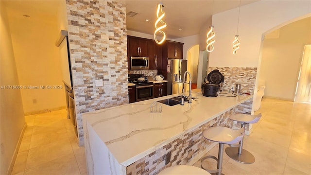 kitchen with a breakfast bar area, decorative light fixtures, a peninsula, stainless steel appliances, and a sink