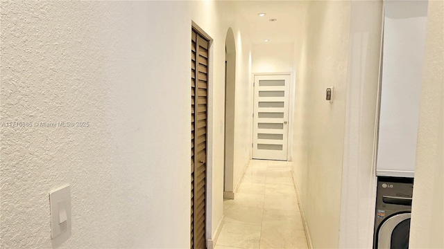 corridor with washer / clothes dryer, a textured wall, and light tile patterned floors