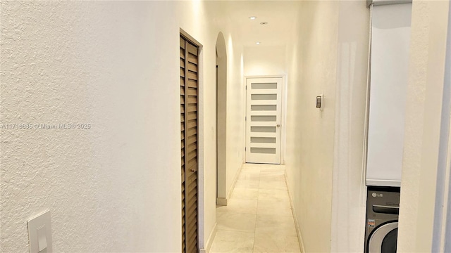 corridor featuring light tile patterned floors, washer / clothes dryer, and a textured wall