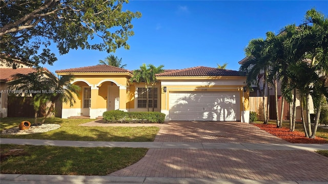 mediterranean / spanish home with decorative driveway, a tiled roof, an attached garage, and stucco siding