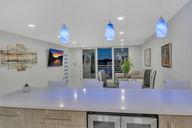 kitchen featuring wine cooler, light stone counters, light brown cabinetry, and hanging light fixtures