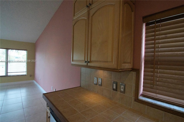 kitchen with tile counters, light tile patterned floors, light brown cabinetry, lofted ceiling, and tasteful backsplash