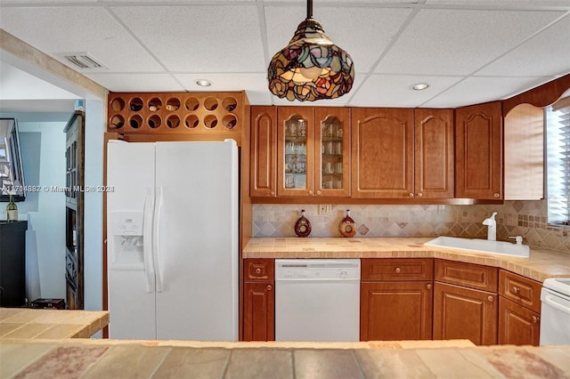 kitchen featuring sink, white appliances, a paneled ceiling, and hanging light fixtures