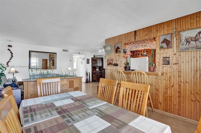 dining room featuring a textured ceiling, light hardwood / wood-style flooring, wood walls, and bar area