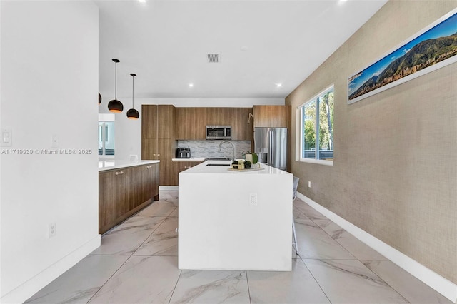 kitchen featuring sink, stainless steel appliances, tasteful backsplash, an island with sink, and decorative light fixtures