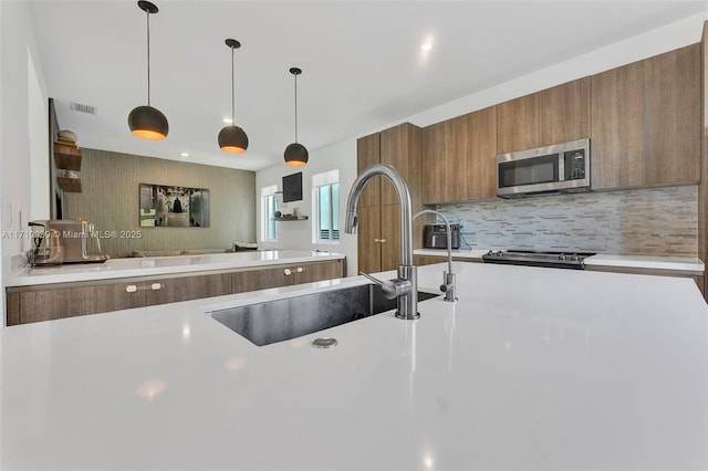 kitchen featuring backsplash, sink, stove, and decorative light fixtures