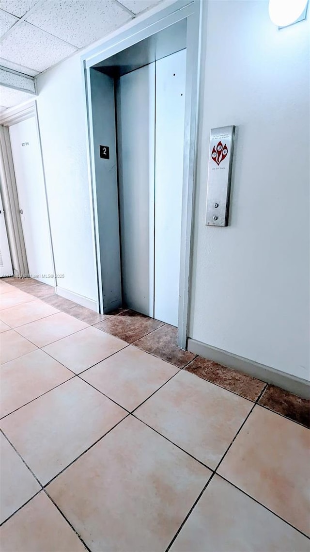 hallway featuring elevator, a drop ceiling, and light tile patterned floors